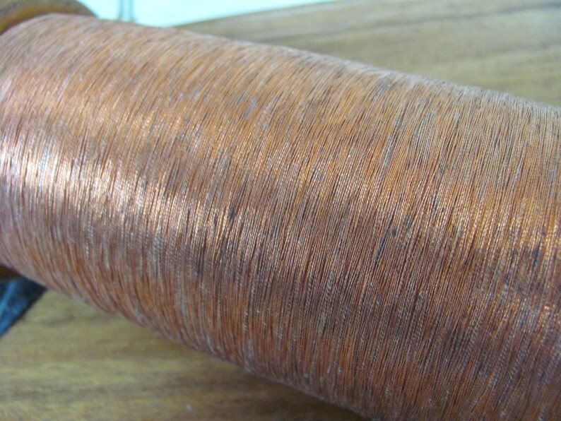 May include: A close-up of a spool of copper wire. The wire is wound tightly around the spool, creating a smooth, shiny surface.