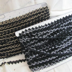 May include: Two spools of black and white trim with a textured woven design. The trim is on a white surface with a star pattern.