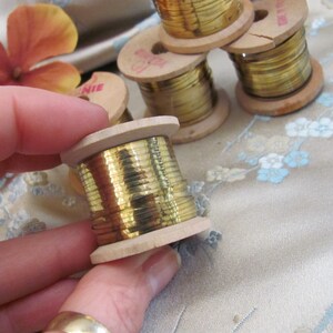 May include: Close-up of a spool of gold metallic thread wound around a wooden bobbin. The spool is being held in a hand.