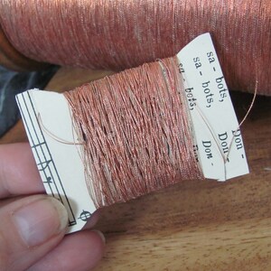 May include: A spool of copper-colored metallic thread with a paper label that reads "sa - bots", "sa - bots", "Don", "Don", "Don - Flow".