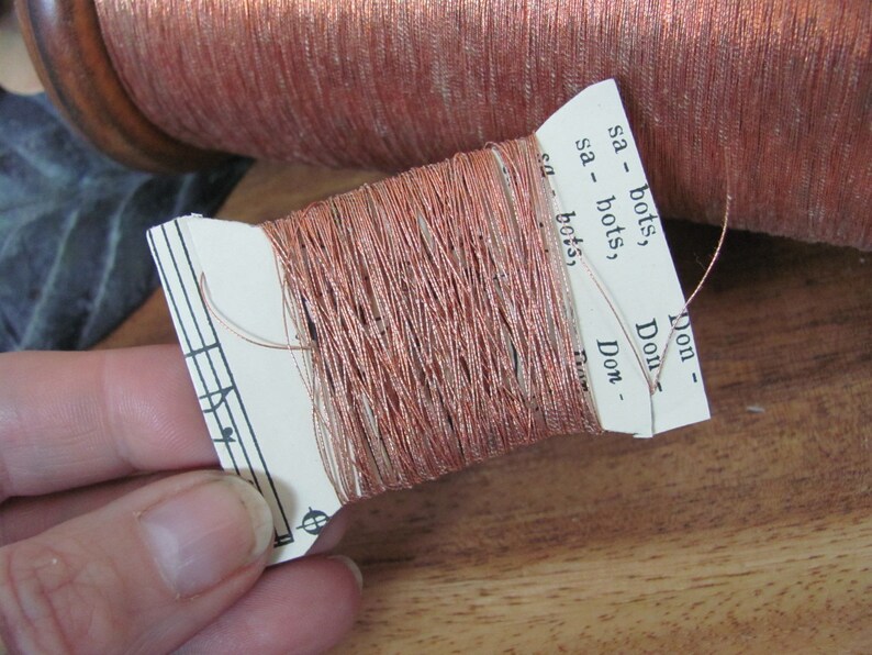 May include: A spool of copper-colored metallic thread with a paper label that reads "sa - bots", "sa - bots", "Don", "Don", "Don - Flow".