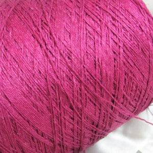 May include: A close-up of a spool of deep pink yarn. The yarn is tightly wound and has a smooth texture.