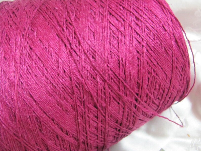 May include: A close-up of a spool of deep pink yarn. The yarn is tightly wound and has a smooth texture.