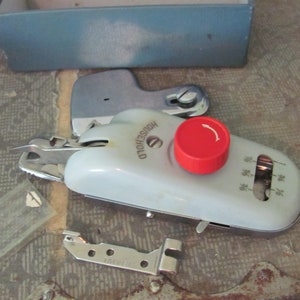 May include: A vintage white and silver sewing machine with a red knob and the words "OLD HOUSEHOLD" printed on the side. The machine is on a patterned surface and includes a variety of attachments.
