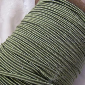 May include: A spool of olive green elastic cord. The cord is wound tightly around the spool, creating a smooth, even surface.