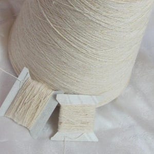 May include: A cone of natural white yarn with two spools of the same yarn, ready for knitting or crocheting.