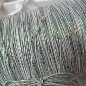 May include: A spool of white elastic cord with iridescent green glitter. The cord is wound tightly around the spool.