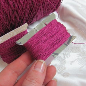 May include: Two spools of deep pink embroidery floss, one on a larger spool and the other on a smaller spool with a decorative paper label.