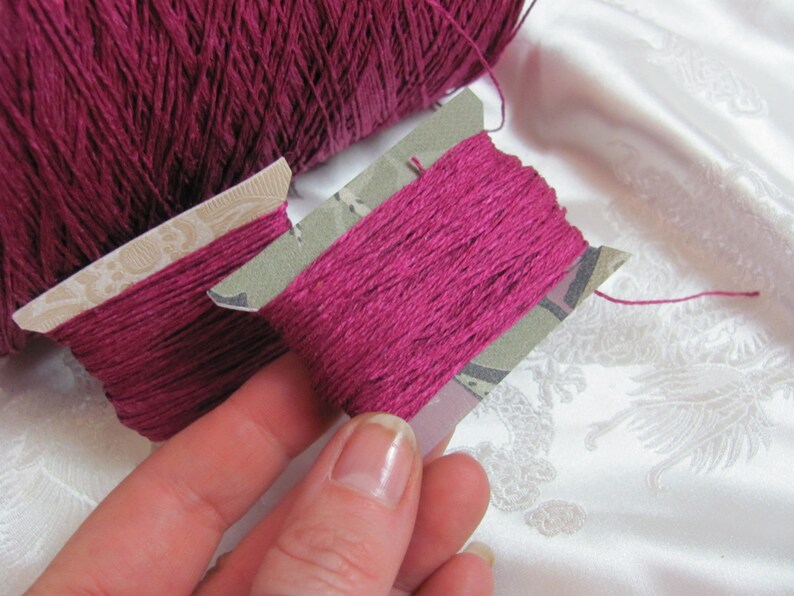 May include: Two spools of deep pink embroidery floss, one on a larger spool and the other on a smaller spool with a decorative paper label.