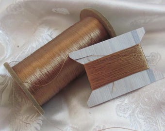 May include: A spool of brown metallic thread wound on a wooden bobbin, with a separate piece of thread on a white card.