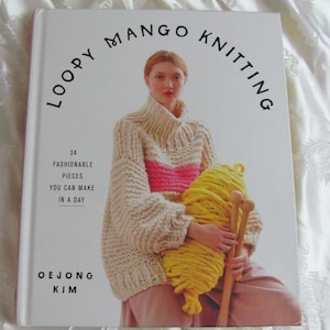 May include: A book titled "Loopy Mango Knitting" with a white cover and a woman wearing a cream, pink, and yellow knitted sweater holding a ball of yellow yarn and knitting needles. The book cover also states "34 Fashionable Pieces You Can Make In A Day" and "Oejong Kim".