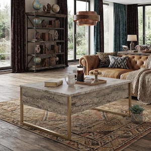 Pode incluir: Uma mesa de centro retangular com tampo em imitação de mármore e acabamento cinzento texturizado, suportada por uma estrutura de metal dourado. A superfície da mesa contém um pequeno livro, um jarro de cerâmica branca e uma prensa francesa.