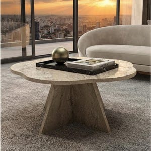 Könnte beinhalten: Ein beigefarbener Steincouchtisch mit einer unregelmäßigen, organisch geformten Tischplatte und einem zentralen Sockel. Auf dem Tisch steht ein schwarzes rechteckiges Tablett mit einer Metallkugel und einem Buch mit dem Text HABITAT 85.