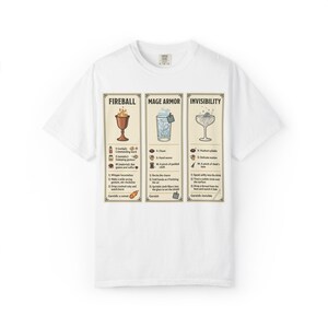 May include: A white short-sleeve t-shirt featuring three vertical rectangular panels with illustrations and text. The panels are titled Fireball, Mage Armor, and Invisibility, each detailing magical spell components, instructions, and a garnish.