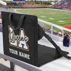 May include: A black portable stadium seat with a backrest and adjustable side straps. The back features a large white and gold graphic with the text LA Queens and the words YOUR NAME printed in white block letters below the main design.