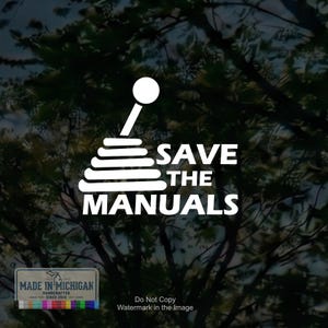 May include: A white vinyl decal featuring a graphic of a manual transmission gear shifter knob and boot, accompanied by the text "SAVE THE MANUALS" in a bold, sans-serif font. The design is presented as a clean, solid white graphic element.