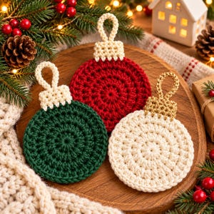 Könnte beinhalten: Drei kreisförmige Häkelornamente in Dunkelgrün, Rot und Creme. Jedes Ornament besteht aus einem strukturierten, runden Körper mit einer passenden gehäkelten Kappe und einer kleinen Schlaufe an der Oberseite zum Aufhängen, gefertigt mit gleichmäßigen Maschen.