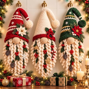 Könnte beinhalten: Drei gehäkelte Wichtel-Wandbehänge mit langen weißen Bärten und spitzen Mützen in Rot, Creme und Grün, verziert mit Weihnachtssternen, Tannenzapfen, Beeren und Schneeflocken. Jeder Wichtel hat eine runde Nase und einen Bommel an der Mützenspitze.