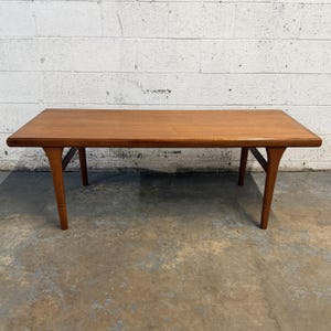 May include: A rectangular wooden coffee table with a smooth, medium-brown finish. The table features a flat top surface with rounded edges and four tapered legs that angle outward from the center, providing a stable base for the furniture piece.