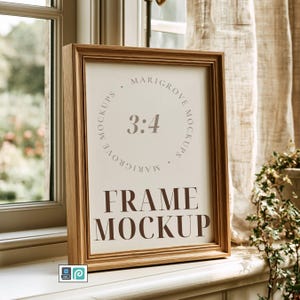 May include: A light wood picture frame containing a white insert with the text 3:4, Marigrove Mockups, and FRAME MOCKUP in dark brown lettering. The frame has a simple rectangular profile and is positioned upright on a flat surface.