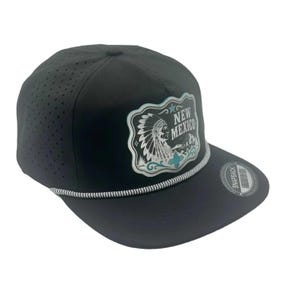 May include: A black snapback cap with perforated side panels and a decorative rope trim across the brim. The front features a graphic patch with a Native American figure in a headdress, the text NEW MEXICO, and a small blue star and sun symbol.