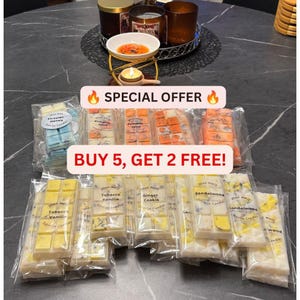 Op de afbeelding: Een verzameling rechthoekige wax melt bars in doorzichtige plastic verpakkingen, met diverse kleuren en labels zoals Tobacco Vanilla, Ginger Cookie en Sandalwood. Een waxinelichthouder met een brandend waxinelichtje staat op de achtergrond.