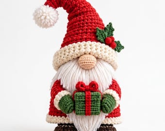 May include: A crocheted gnome figurine wearing a red hat with a white pom-pom and a cream-colored brim. The gnome has a long white yarn beard, a beige nose, green mittens, and dark brown shoes, while holding a small green gift with a red ribbon.