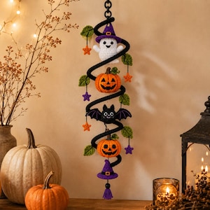Peut inclure: Une suspension murale en crochet verticale composée d'une spirale noire ornée d'un fantôme blanc avec un chapeau violet, deux citrouilles orange, une chauve-souris noire, des feuilles vertes et des petites étoiles orange et violettes.