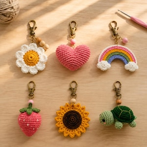 Pode incluir: Seis porta-chaves de croché com uma margarida branca, um coração rosa, um arco-íris com nuvens, um morango rosa, um girassol amarelo e uma tartaruga verde. Cada item está preso a um mosquetão de metal cor de bronze com contas de madeira.