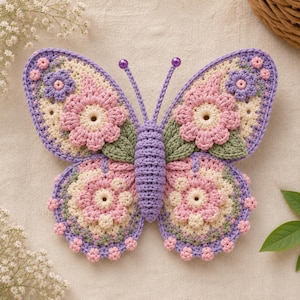 May include: A handcrafted crochet butterfly decoration featuring a lavender body with two antennae topped by purple beads. The wings are adorned with cream, pink, and lavender floral motifs, accented with small green leaves and lavender borders.