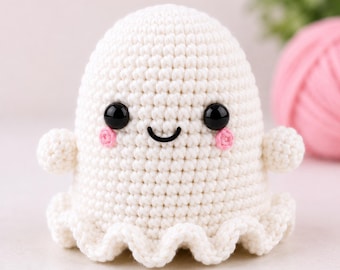May include: A white crocheted ghost figure with a rounded top, small arms, and a ruffled base. The ghost features two black plastic bead eyes, a stitched black curved mouth, and two small pink embroidered circles on the cheeks for blush.