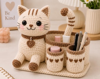 May include: A beige and brown crochet cat desk organizer featuring a seated cat figure with a heart charm collar, a curved tail, and two cylindrical pen holders decorated with small brown heart patterns, all set on a rectangular base.