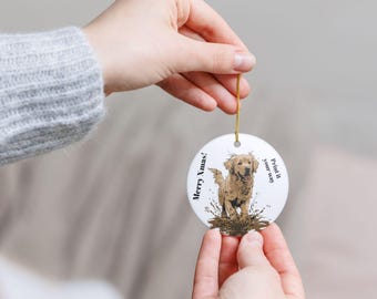 May include: A round, white Christmas ornament featuring a golden retriever dog in a muddy puddle. The ornament has the text "Merry Xmas!" and "Print it your way" in black. A gold string is attached for hanging.