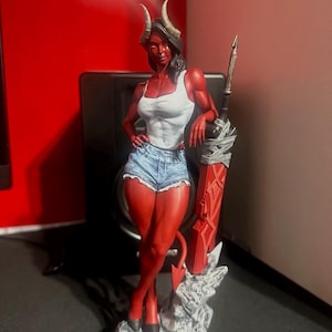 以下が含まれることがあります： 角が生えた赤い肌の悪魔の塗装済み樹脂製フィギュア。白いタンクトップと青いデニムのショートパンツを着用している。灰色の岩のような台座の上に立ち、金属製の柄が付いた大きな赤い剣に寄りかかっている。長い尖った尻尾が特徴。
