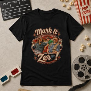 Może przedstawiać: Czarny t-shirt z nadrukiem graficznym przedstawiającym trzy postacie na kręgielni. Tekst "Mark it" znajduje się nad postaciami, a "Zero" jest wydrukowane poniżej wraz z kulą do kręgli i kręglami. Wzór zawiera akcenty w kształcie gwiazdek.