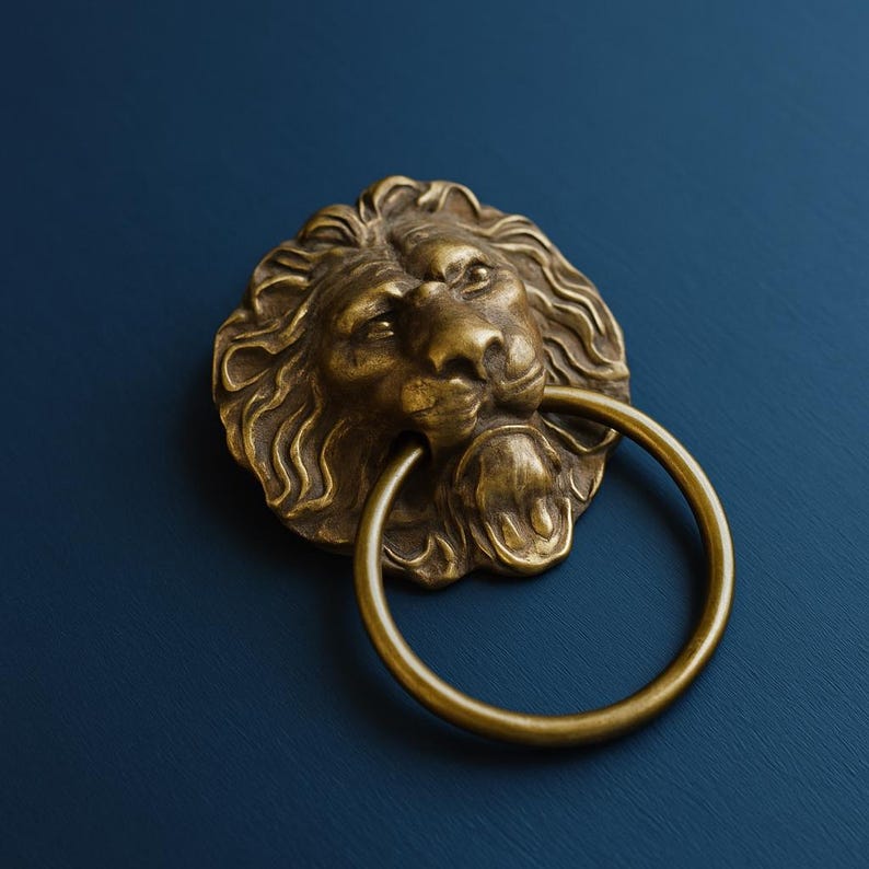 Pu&ograve; includere: Un battente per porta in metallo color ottone raffigurante una scultura dettagliata di testa di leone con una criniera fluida e un anello circolare tenuto nella bocca del leone. La ferramenta ha una finitura metallica con aree scure.