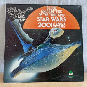 May include: A vinyl record album cover featuring a blue and yellow spaceship against a black background with stars. The album title is "Close Encounters of the Third Kind Star Wars 2001 A Space Odyssey" and the text "The Now Sound Orchestra Present Music From" is at the top left corner.