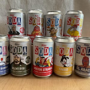 May include: A collection of Funko Soda collectible figures in soda can packaging. The cans feature various characters, including Energizer Bunny, Silent Bob, Doctor Strange, and Yakko. The cans are silver with colorful graphics.