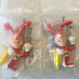 May include: Two red and white plastic figurines of a cartoon character holding a yellow drill. The character has large ears, a red suit, and a white collar. The text "12 BVG" is visible on the packaging.