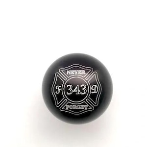 May include: A spherical black gear shift knob featuring a white engraved Maltese cross emblem. The center of the cross displays the number 343, with the letter F on the left, D on the right, and the words NEVER FORGET inscribed above and below.