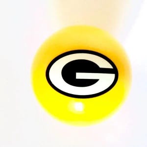 May include: A bright yellow spherical object featuring a centered logo consisting of a white letter G with a thick black outline. The design is printed clearly on the smooth, rounded surface of the ball, which has a glossy finish and reflects light.