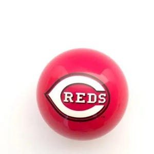 May include: A smooth, spherical red ball featuring the white and red Cincinnati Reds logo in the center. The logo consists of a large white letter C with the word REDS printed in white block letters inside, all outlined in black.