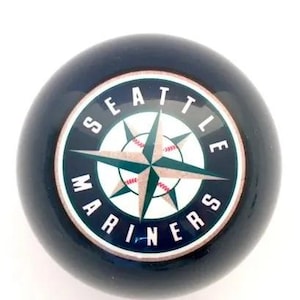 May include: A dark navy blue spherical object featuring the Seattle Mariners logo in the center. The logo displays a white compass rose with teal and silver accents, overlaid on a baseball graphic, surrounded by the text Seattle Mariners.