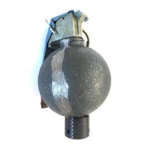May include: A spherical hand grenade with a textured dark gray surface featuring a vertical brushed metal stripe. The top assembly is made of light blue and silver metal with a pull ring, and the base has a black cylindrical knurled component.
