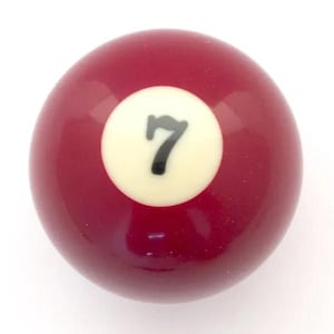 May include: A smooth, spherical billiard ball with a glossy maroon finish. Centered on the ball is a circular white field containing the number 7 printed in a bold, black, sans-serif font. The surface is reflective and uniform in color.