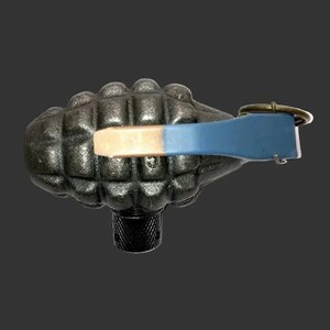 May include: A dark gray, textured, oval-shaped object resembling a hand grenade with a grid pattern. It features a blue and metallic-colored lever mechanism on top, secured by a circular metal ring, and a cylindrical, knurled black base at the bottom.