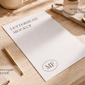 May include: A white letterhead mockup sheet featuring the text LETTERHEAD MOCKUP at the top and an oval logo with the letters MF at the bottom. A gold pen lies to the left of the paper, which is positioned on a textured beige surface.
