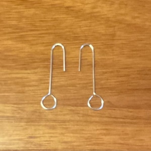 May include: A pair of silver earrings with a simple, curved design. The earrings are made of thin metal and have a small loop at the top for attaching to an earring hook.