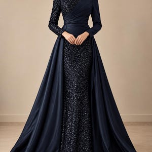 May include: A floor-length navy blue gown featuring a high neckline and long sleeves. The bodice and skirt are covered in dark sequins, while a smooth, solid navy blue fabric creates a draped, wrap-style overlay across the torso and waist.