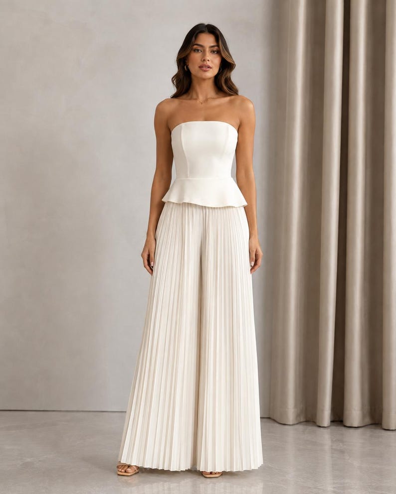May include: A white strapless jumpsuit featuring a fitted bodice with a peplum waist detail and wide-leg trousers with vertical pleats throughout the length of the pants. The garment is a solid off-white color with a clean, structured silhouette.